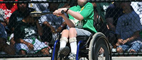 boy in a wheelchair swinging a bat at a baseball